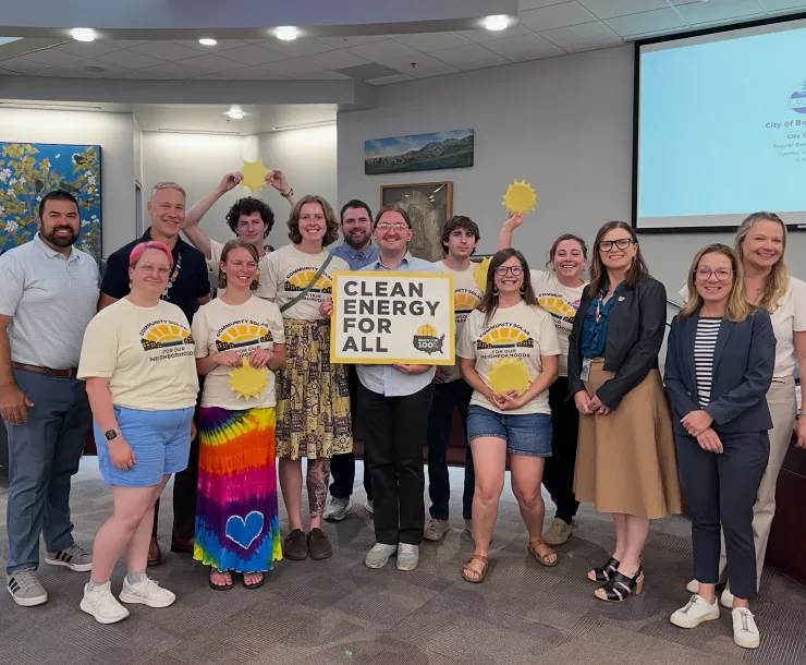 Picture of Sierra Club activists wearing matching solar shirts holding a sign that says Clean Energy For All and sunshines standing with the Boise Mayor and City Councilors in the Council Chambers