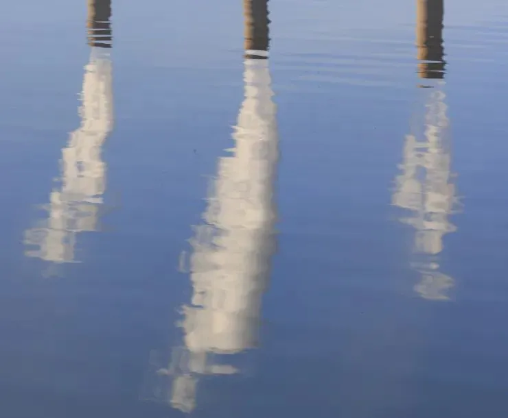 Image of three power plant smokestacks reflected by a body of water.