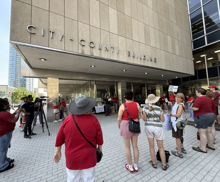 A group of over 20 people outside the city-county building in Indianapolis. There is a cameraman there filming. Some are holding signs to protect Eagle Creek.
