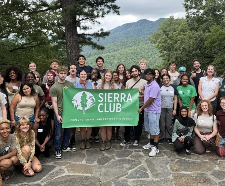 A group of people pose for a photo in western North Carolina, holding a Sierra Club banner with a mountain landscape behind them