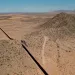 Aerial photo of a large stretch of border wall cutting through scrubby desert landscape.