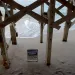 View looking through the stilts of a house toward the Atlantic Ocean, with waves lapping up to a Coldwell Banker real estate sign in the sand at Nags Head, North Carolina.