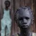 This July 14, 2017 photo shows two of the 40 statues spread throughout the grounds, titled "Children of Whitney" by Woodrow Nash, in front of one of the slave cabins at the Whitney Plantation in Edgard, La.