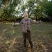 Ole Schell stands in a grassy field with a plaid shirt and his arms spread, smiling and looking at the sky.