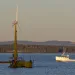 Offshore wind turbine floats off the coast of Maine with a lobster boat and forest in the background