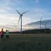 Unrecognized engineers wearing safety helmets working in wind turbine farm during the evening.
