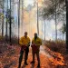 Two men dressed in yellow PPE and holding fuel canisters set a prescribed burn to a forest in Southwest Georgia.