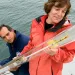Amy Bower and an engineer hold a subsurface buoy, while standing on a ship deck, the ocean behind them.