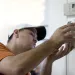 A man installs a thermostat in a home. 
