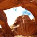Two connected red-orange sandstone arches in front of a blue and white cloudy sk