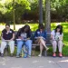 4 people sit on a bench writing on pieces of paper