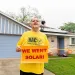 A man holds a "We Want Solar" sign outside his home.