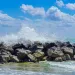 Waves crashing on a rock jetty in Dania Beach, Florida, with puffy clouds in the background