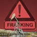 background photo of fracking sign with fracking operation in front.