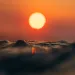 A water-level view of small waves and the sun against an orange sky