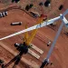 Aerial photo of a white wind turbine over a red dirt area, with a yellow crane attached and some cars scattered underneath