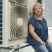  Anne Pappas sits next to her heat pump, installed on the side of her gray and white mobile home.