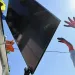 A worker hands off a solar panel being installed by another worker