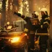 Two firefighters in a smoky forest look at a laptop and strategize next to an all-terrain vehicle laden with equipment.
