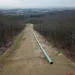 A clear-cut section of forest with pipeline laying in the dirt.