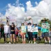 A group of protestors stand outside in sunny Florida, holding signs