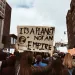 A crowd of people at a protest with someone holding a sign that reads, "It's a planet, not an empire."