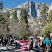 A line of protesters hold signs and an upside-down US flag in Yosemite National Park in front of a waterfall.