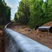 A pipeline running through a dug-up trench through a forest.
