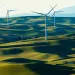 Three windmills stand to attention in a lush, rolling green field, with hills and mountains in the background