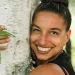 Leah Penniman wears a black top and smiles at the camera while hugging a white-barked tree.