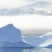 A large iceberg floats just off shore in Baffin Bay, Greenland. A bank of fog lies between the iceberg and the mountains in the background.