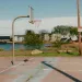  A basketball court at water level with houses lined along the shore.