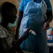A woman in Uganda wearing a printed dress is handing a nurse a paper.