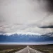 Looking down Nevada's Route 50, with no cars, snowy mountains in the background, and a cloudy sky