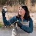 Fran Silva-Blayney stands in the middle of a river, wearing waders and holding up a water sample.