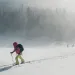 A backcountry skier slides uphill in the snow through a heavy mist.