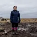 Charlene Carl, in waders, stands on muddy ground where her home used to be in Newtok, Alaska.
