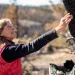 Katie Fite, wearing a red vest, reaches out to touch a burned juniper tree.