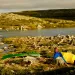 A woman stands by a yellow and blue tent and a green canoe in front of the Inukjuak River in Quebec's Tursujuq National Park.