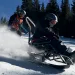 Two people are flying down a ski slope with an Enabling Technologies Dynamique Bi Ski.