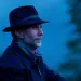 A dark photo of John Luther Adams in a fedora looking off in the distance.