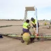 Workers in reflective gear make adjustments to a large geometric-shaped piece of equipment on an airfield. 