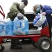 People in face masks unloading bottles of water from a car and on to a red hand truck