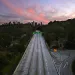 An empty highway surrounded by greenery seen from the air, reaching into a pink purple sunset.