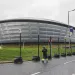 A futuristic silver looking building, like a canoe-shaped pillow of metal against green grass and a gray sky