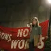 Young woman speaking into a megaphone in front of a red banner that reads "Actions, not Words."