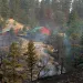 Charred earth and trees smoke with a red house in the background.