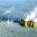 Yellowish gray smokestacks emerging from a rolling white blanket of fog