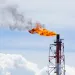 A bright orange flame and smoke coming out of an oil well against a light blue sky