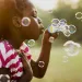 Black girl blowing bubbles in a green and verdant landscape